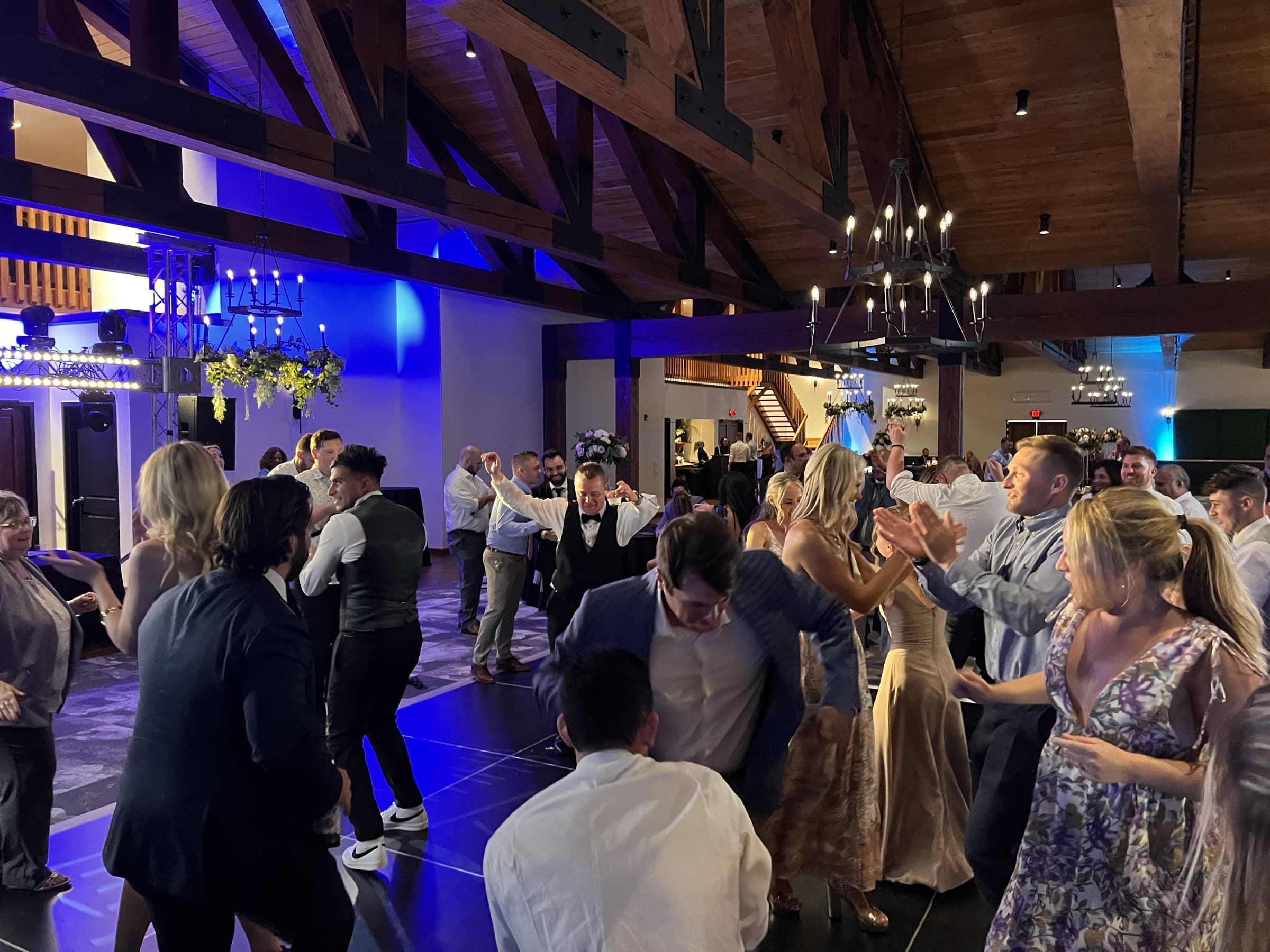 A packed wedding dance floor under exposed timber trusses and chandeliers
