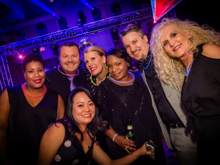 Guests in glow necklaces pose on the dance floor under truss-mounted lighting at a company party