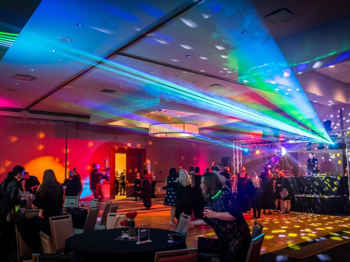 Lasers sweep a hotel ballroom as guests dance beside the truss rig and DJ booth at a company party