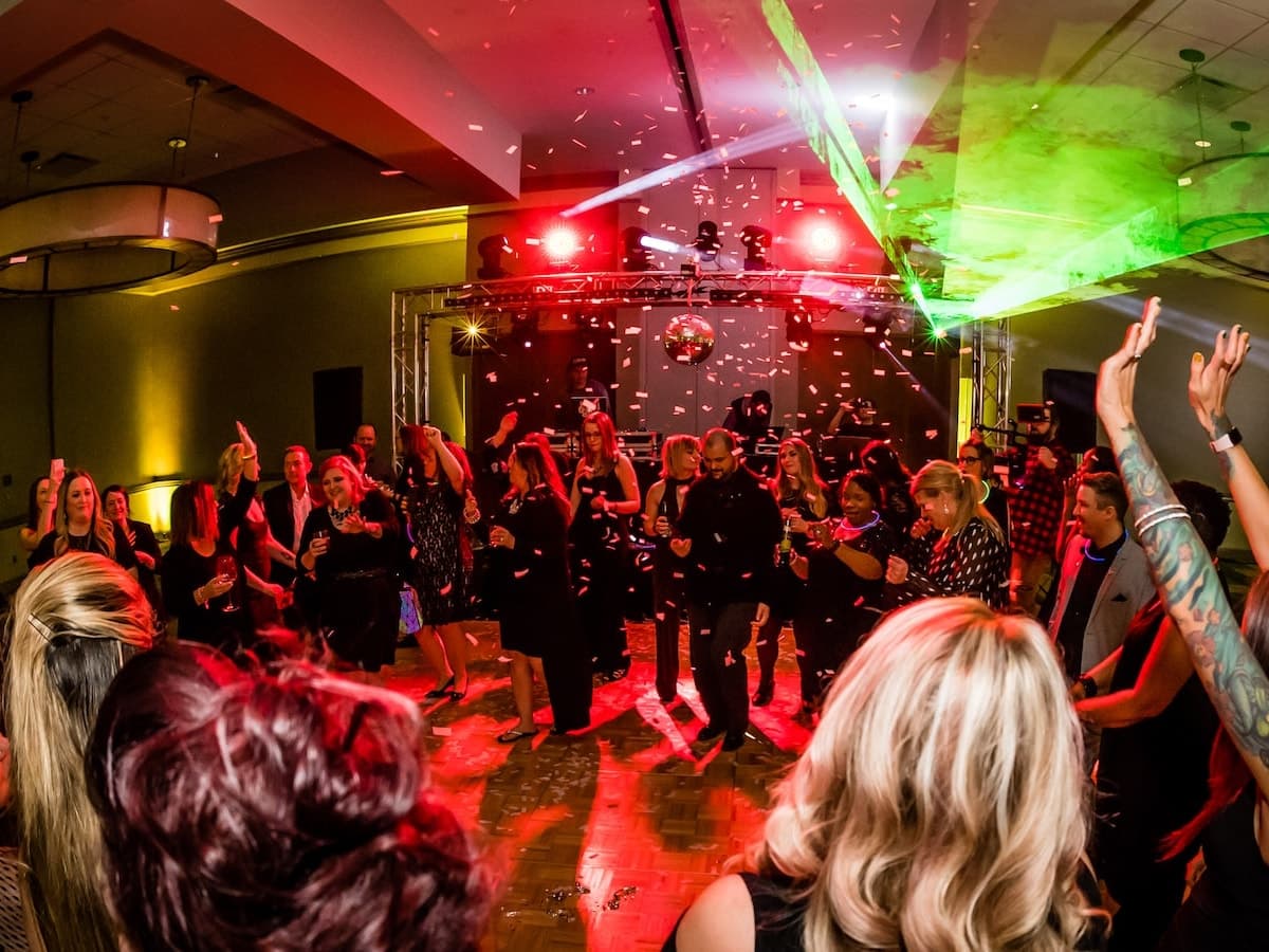 Confetti falls on a packed dance floor at a company party, truss lighting and mirror ball behind