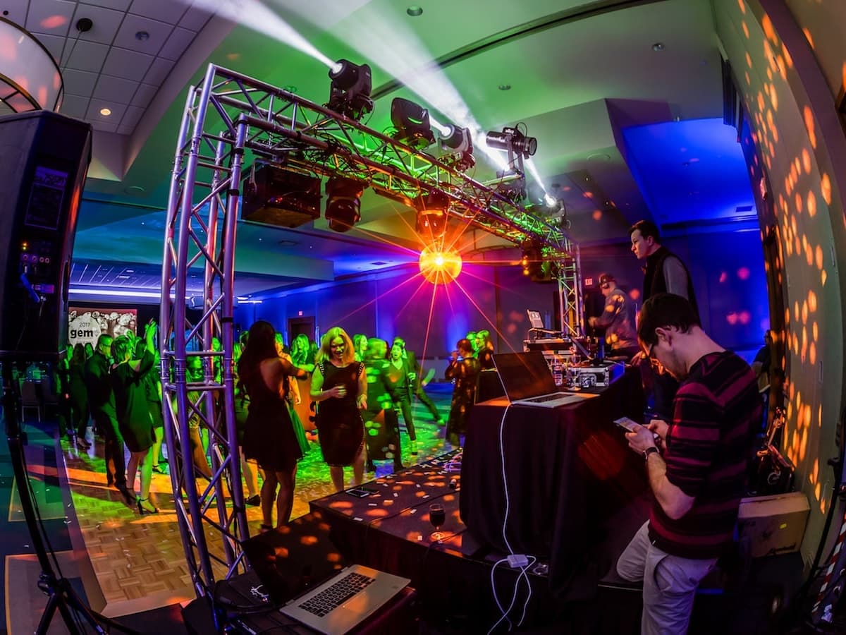 View from the DJ booth under the truss rig as dancers fill a green-lit ballroom floor
