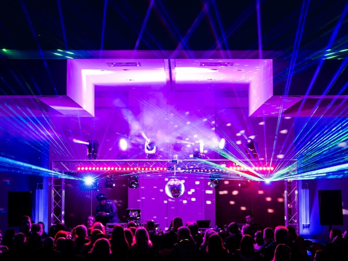 Purple-lit truss rig with moving heads, lasers and a mirror ball over a crowded dance floor