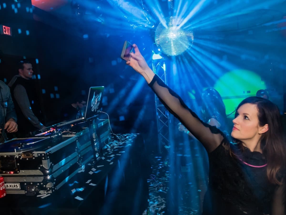 A guest snaps a phone photo of the mirror ball beside the DJ booth in blue haze