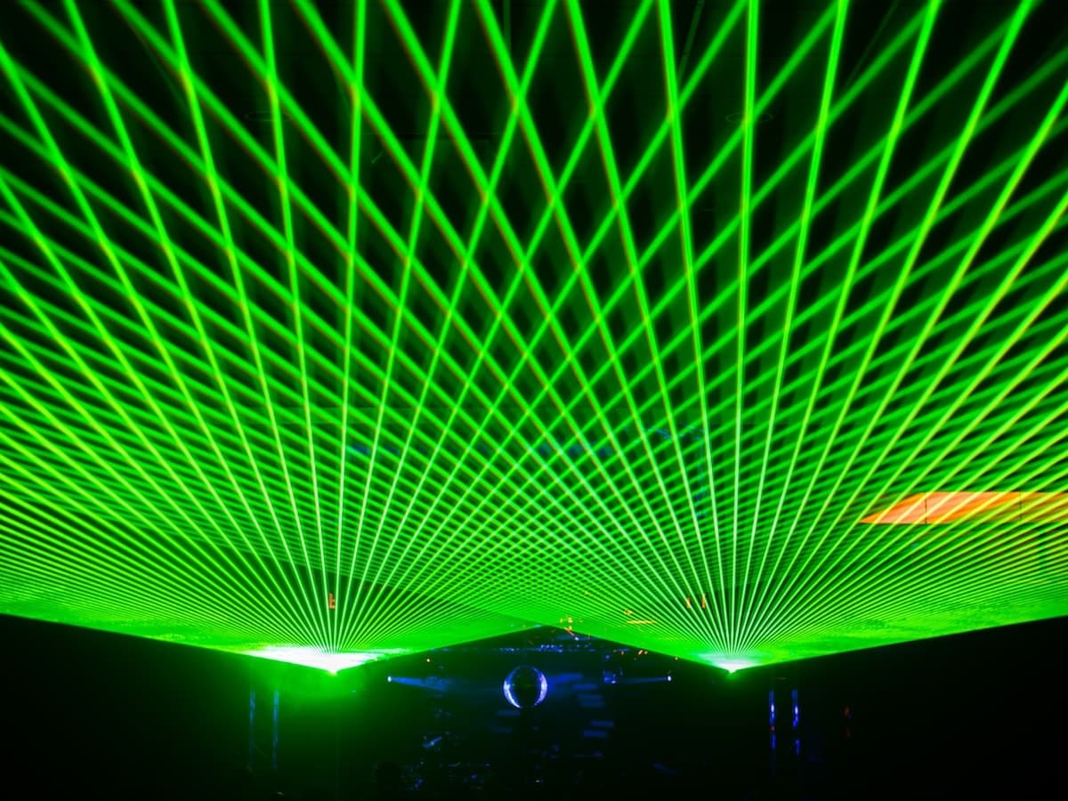 Green laser lattice filling the ceiling above a mirror ball and DJ setup