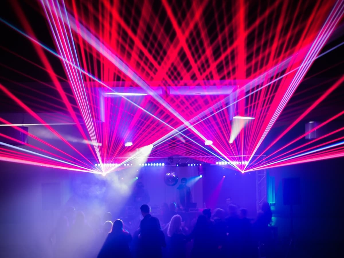 Red laser beams fan through haze over a crowd, LED bars and a mirror ball on the truss