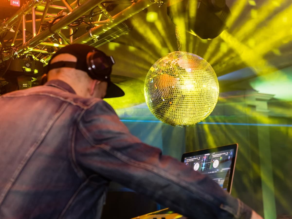 DJ in headphones at the laptop beneath a gold-lit mirror ball and truss lighting