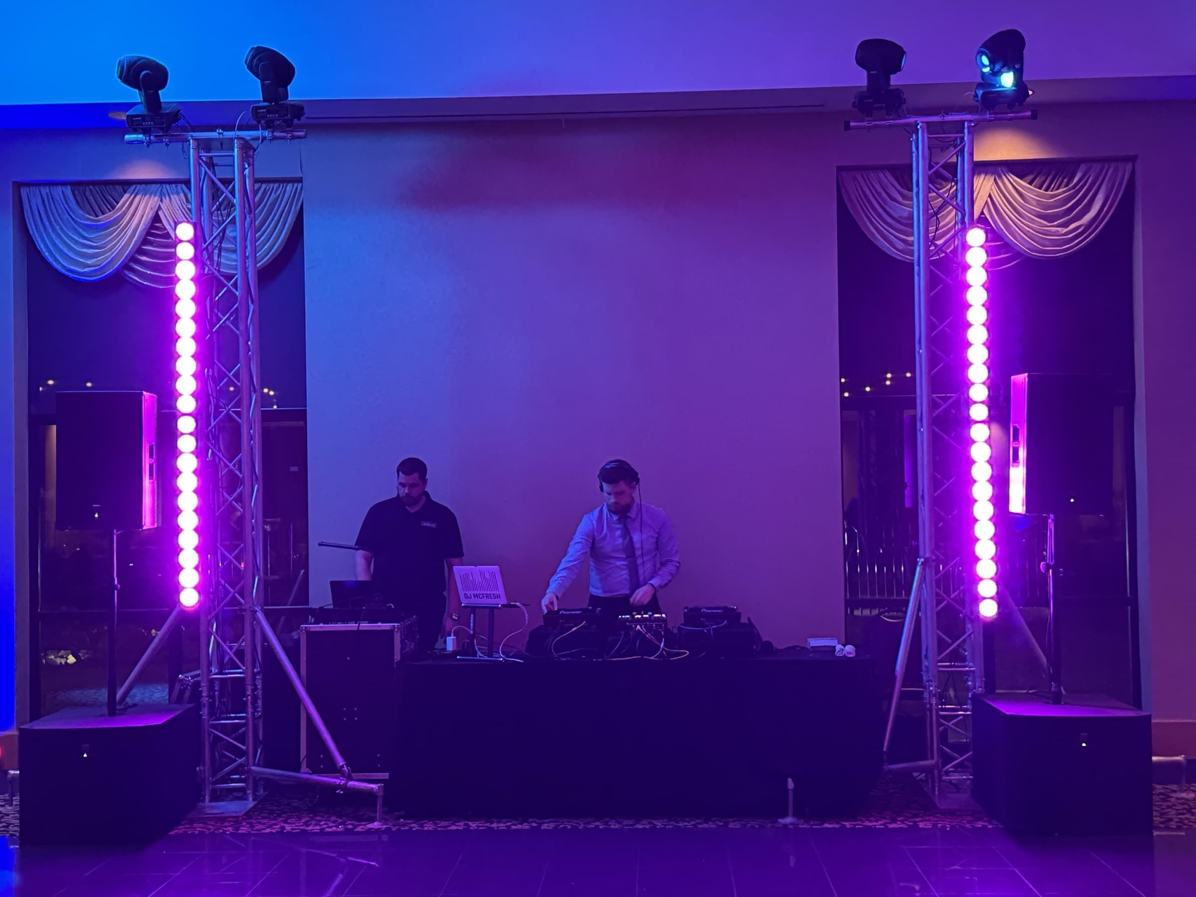 Gold setup: twin truss totems with moving heads and pink LED bars flank the DJ table in a draped ballroom