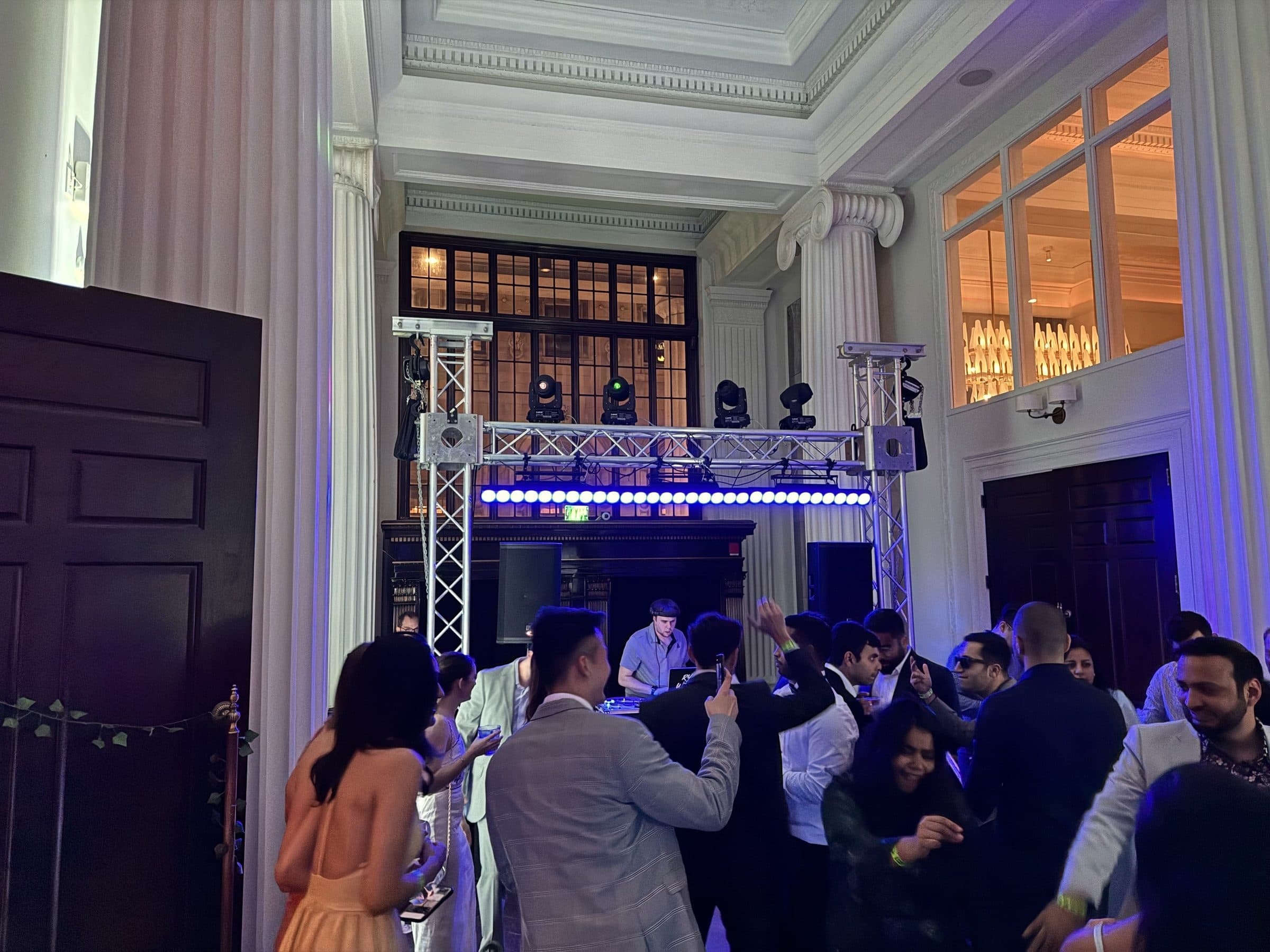 Gold setup: guests dancing beneath the goalpost truss, moving heads and blue LED bar between classical columns