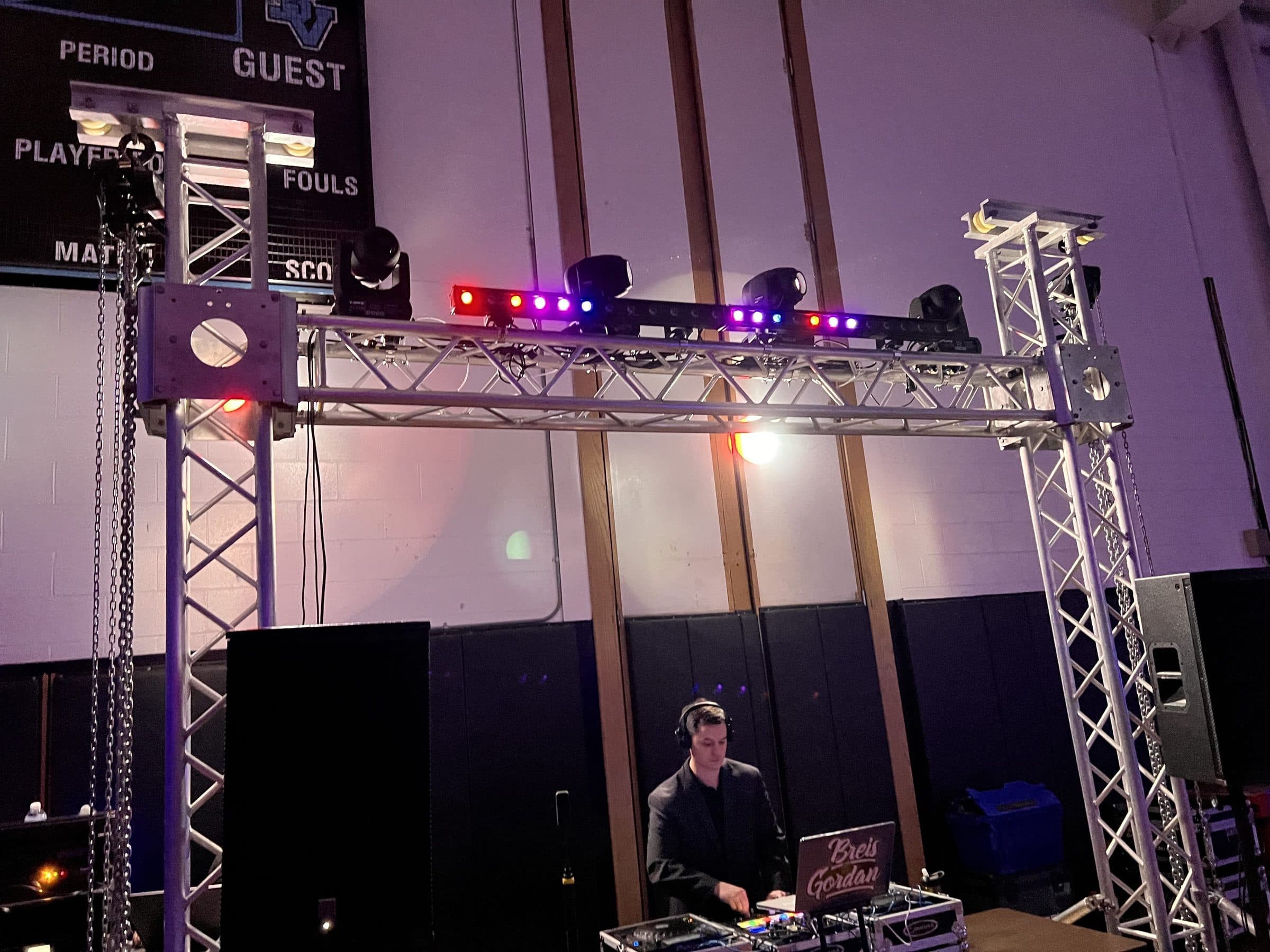 Gold setup in a school gym: goalpost truss with four moving heads and an LED bar above the DJ booth