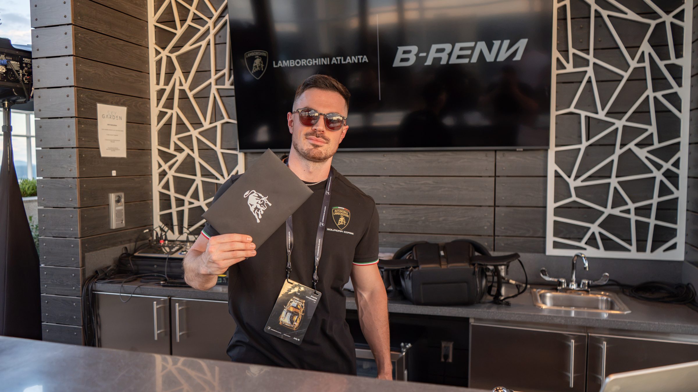 DJ B-Renn in headphones cueing the next track at a rooftop DJ booth above a city skyline