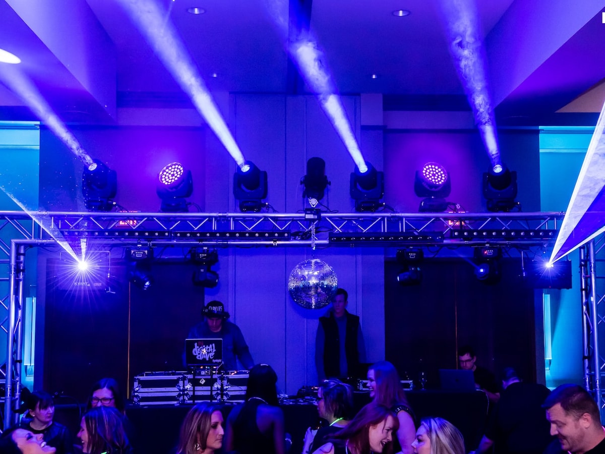 Seven moving-head beams cut through blue haze above a truss rig and mirror ball as the DJ plays