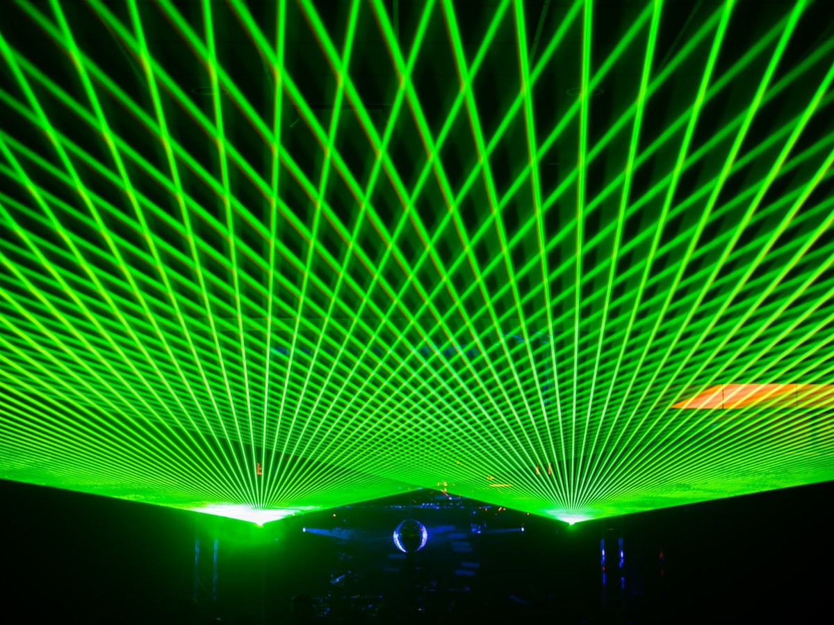 Green laser lattice filling the ceiling above a mirror ball and DJ setup